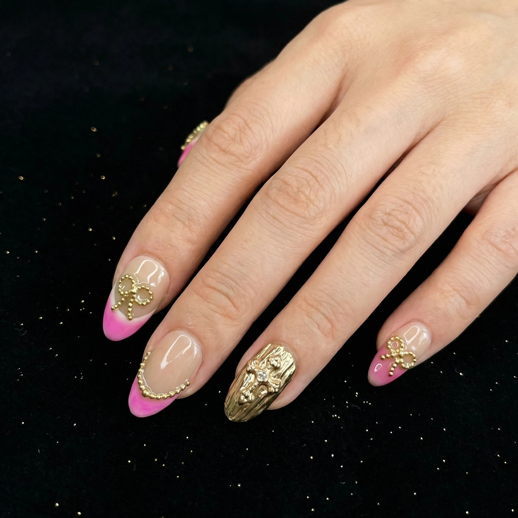 Pink French tip press-on nails on hand against black background, nude base with gold sparkle
