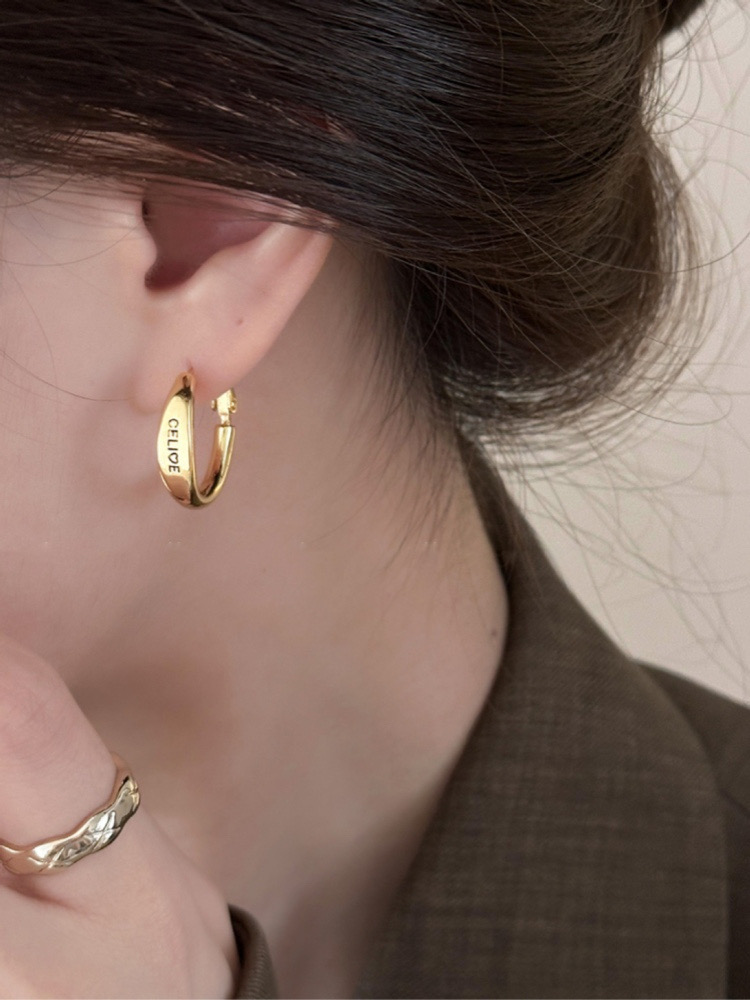 Close-up of gold tone hoop earring worn on ear with brown blazer