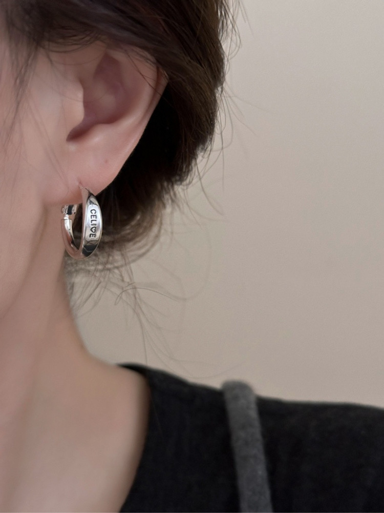 Close-up of silver tone engraved hoop earring worn on ear