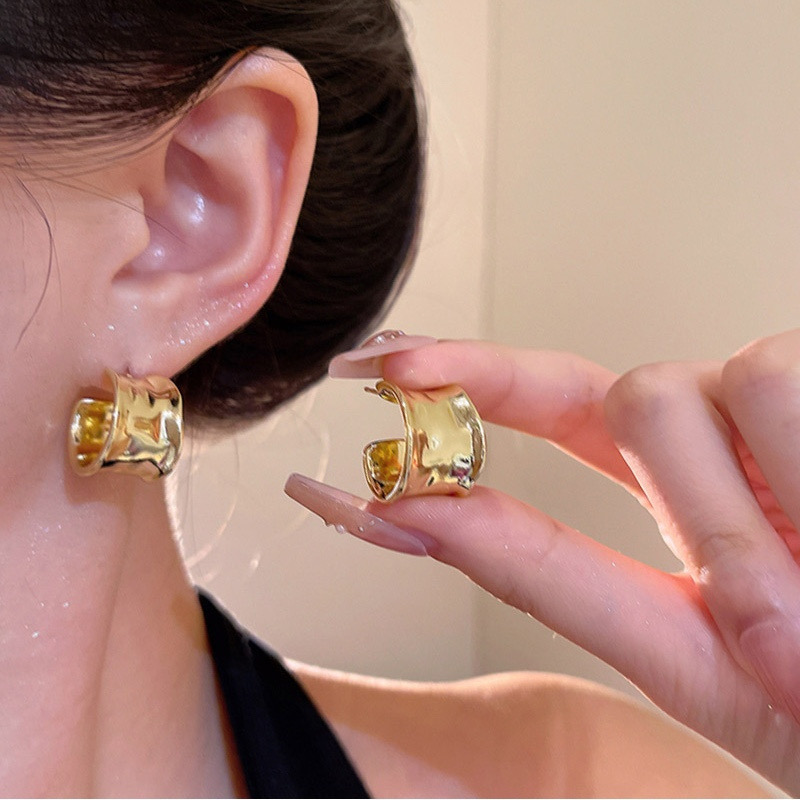 Model wearing gold sculptural wide hoop earring and holding matching gold earring