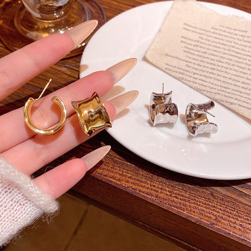 Gold and silver sculptural wide hoop earrings displayed in hand with polished curved design