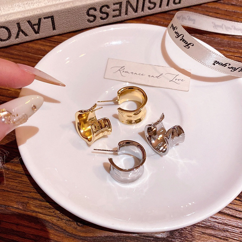 Gold and silver chunky curved hoop earrings arranged on a white ceramic plate