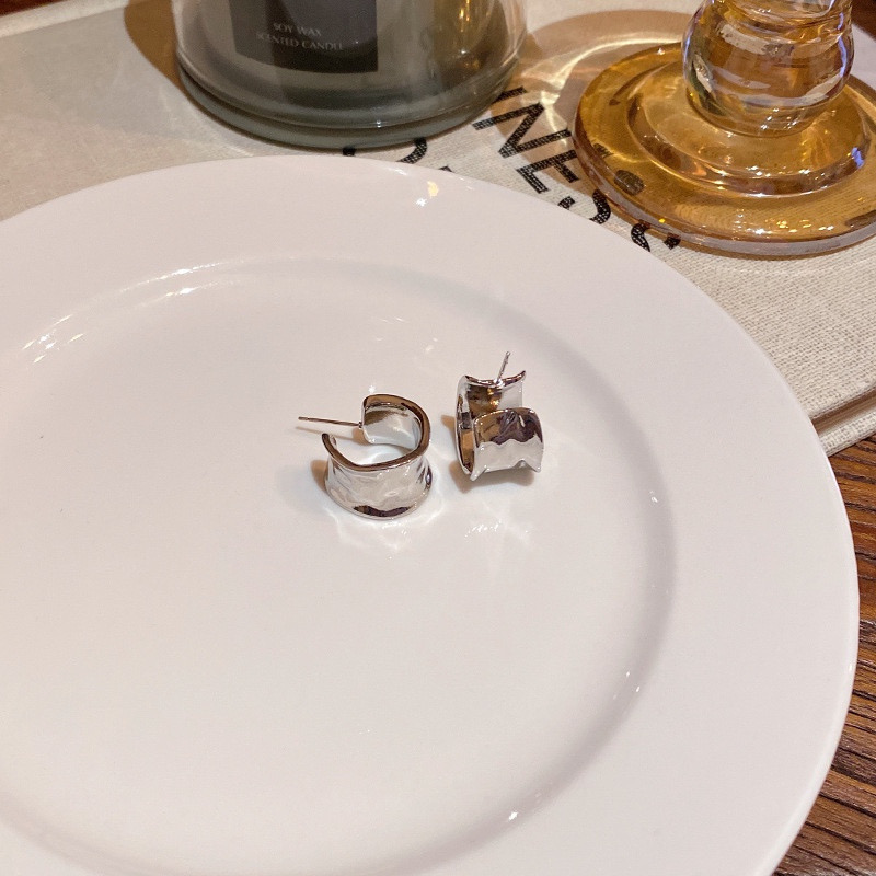 Pair of silver sculptural wide hoop earrings displayed on a white plate