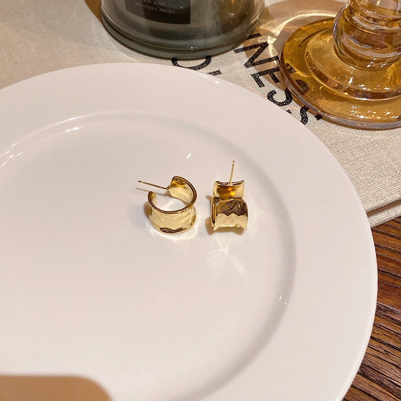 Pair of gold sculptural wide hoop earrings displayed on a white plate
