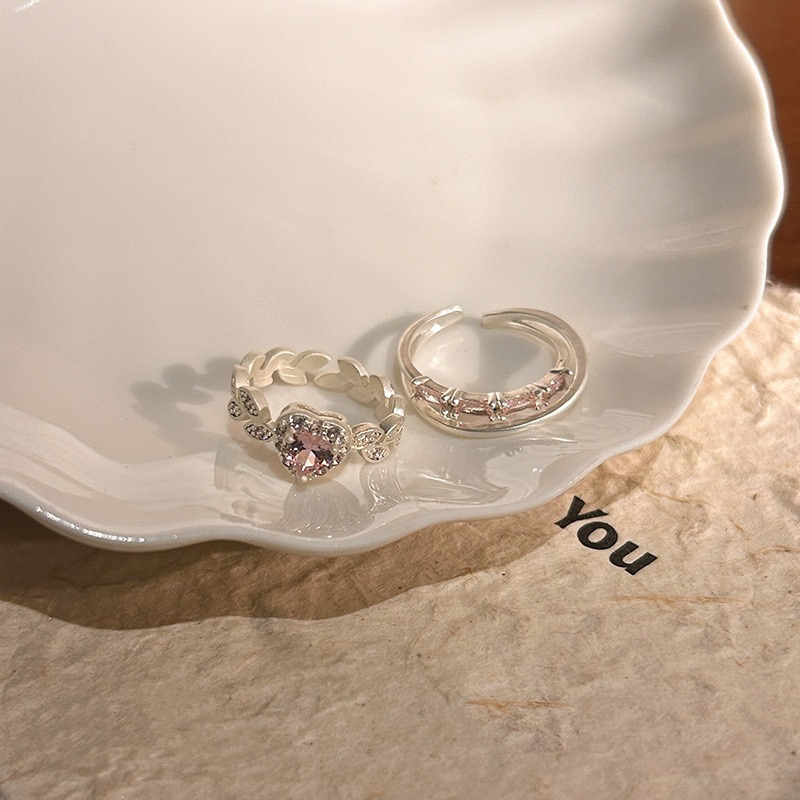Pink heart rhinestone ring and curved silver ring styled together on a finger