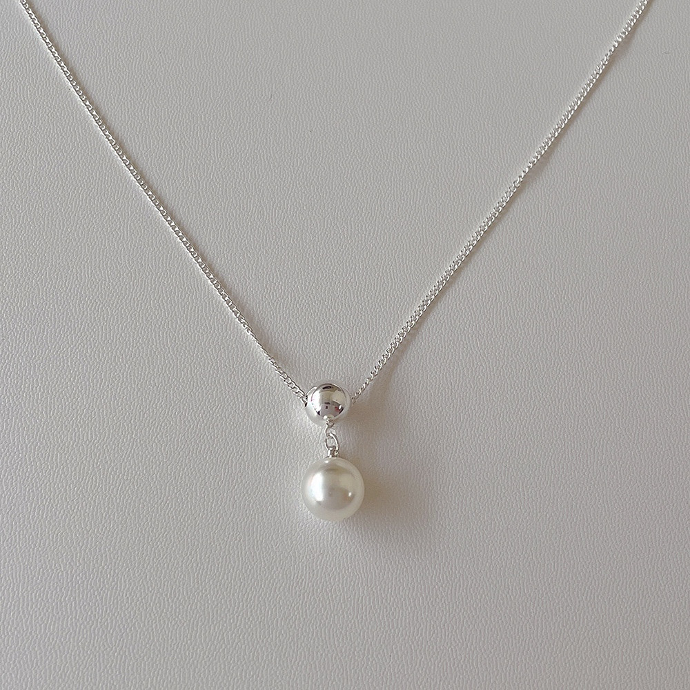 Silver-tone ball and white faux pearl pendant necklace displayed on a light background