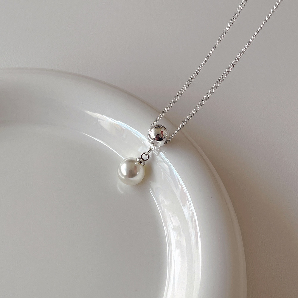 Detailed view of polished silver ball and white faux pearl drop pendant