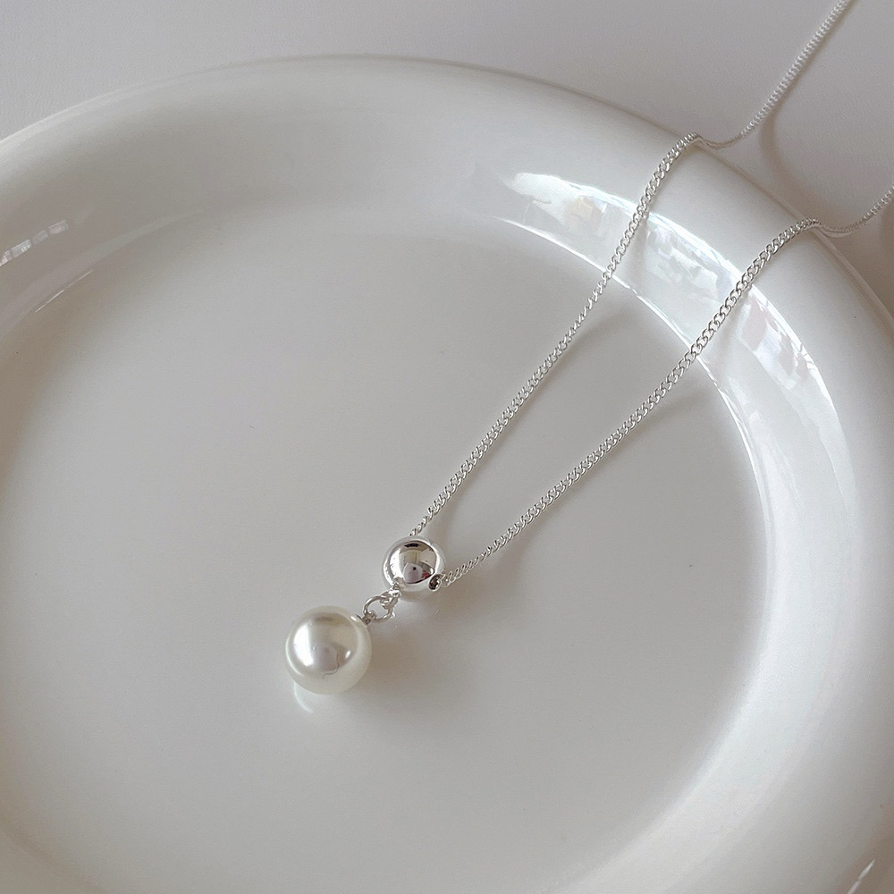 Close-up of silver ball faux pearl necklace pendant displayed on a white ceramic plate