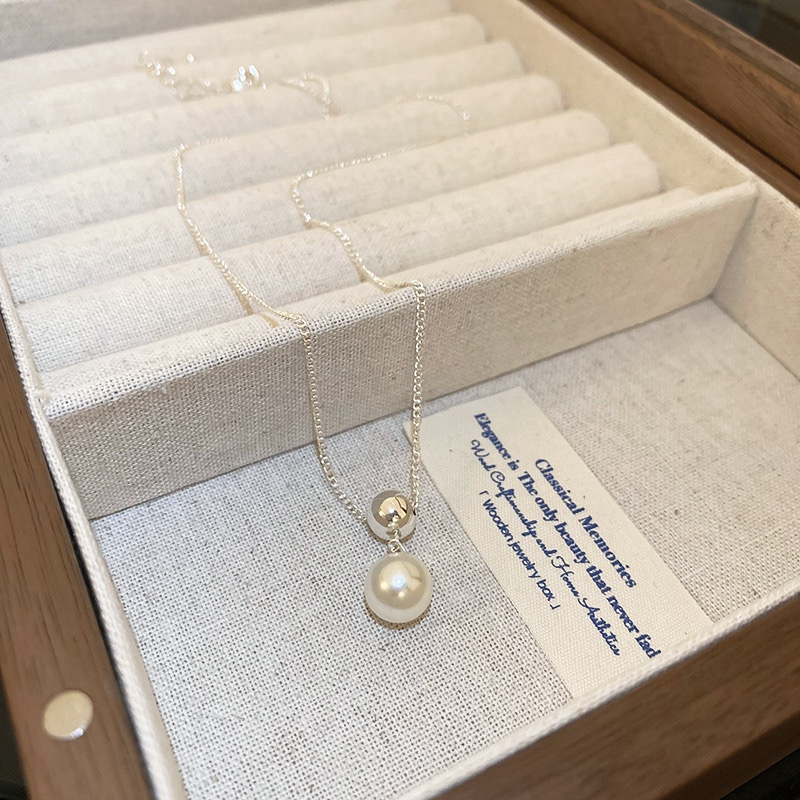 Close-up of a silver-tone faux pearl pendant necklace styled with a white outfit