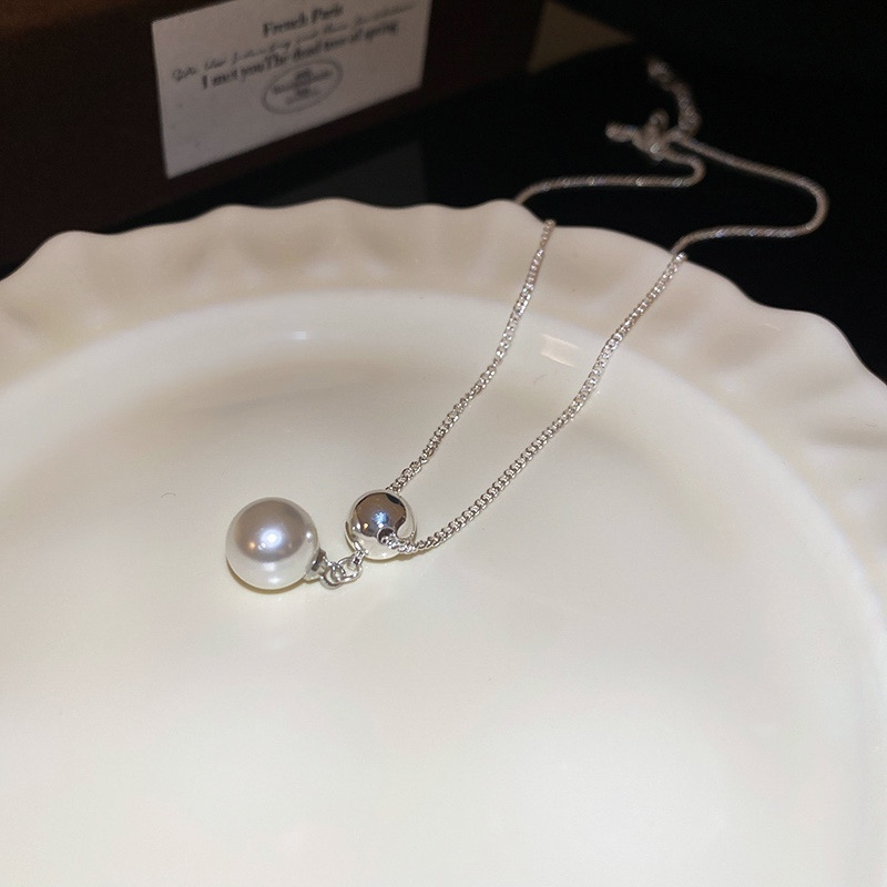 Silver ball faux pearl pendant necklace arranged on a white decorative plate