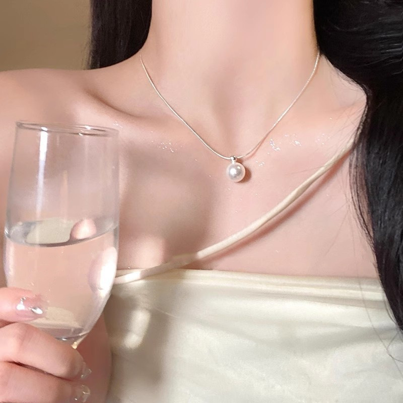 Woman wearing a silver-tone faux pearl pendant necklace with a champagne-colored top