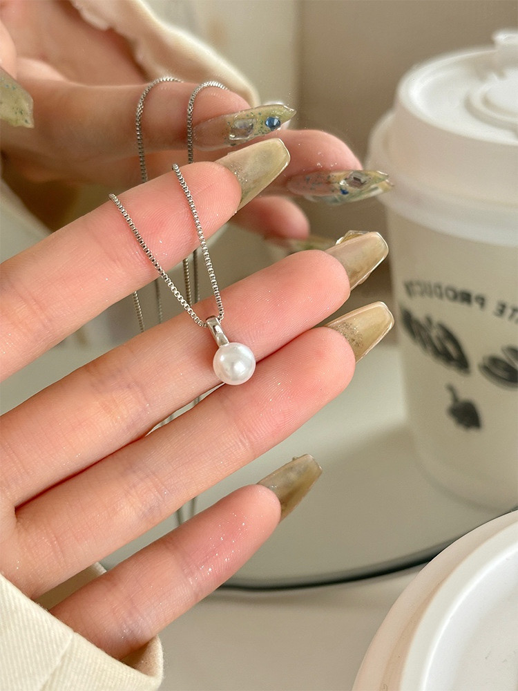 Hand holding a delicate silver-tone necklace with a single white faux pearl pendant