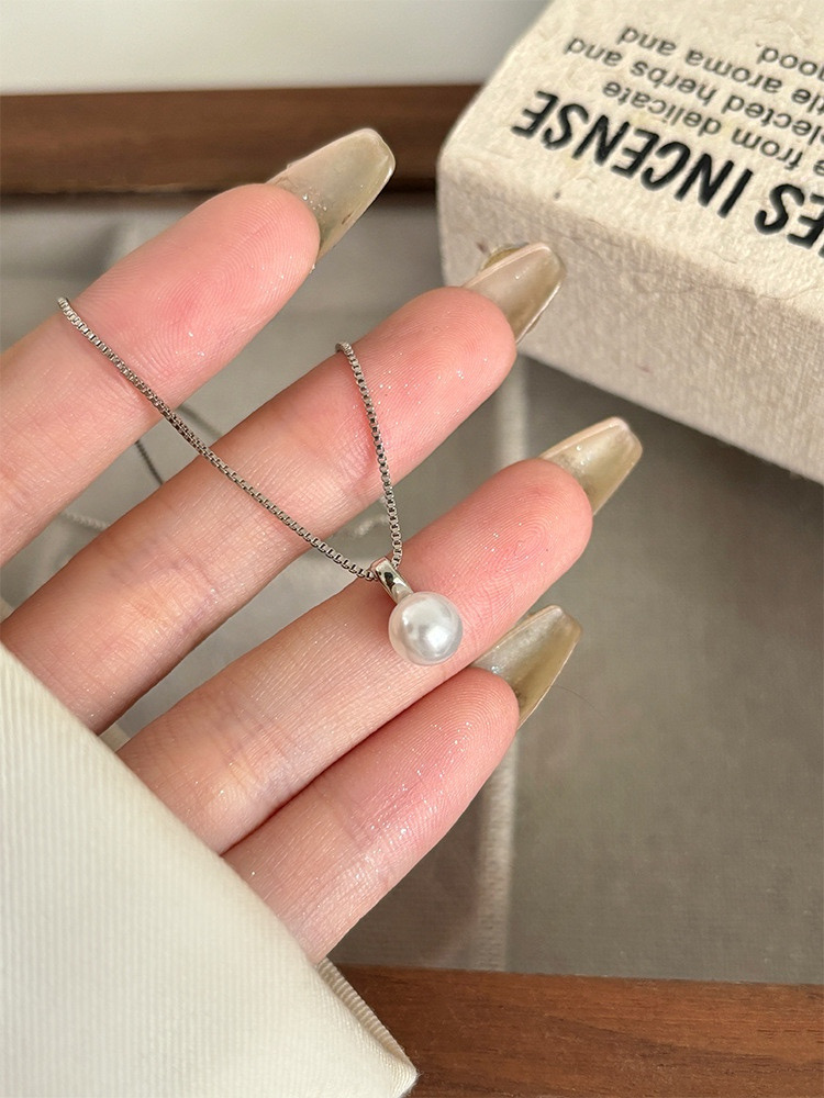 Detailed view of a single white faux pearl pendant hanging from a silver-tone chain