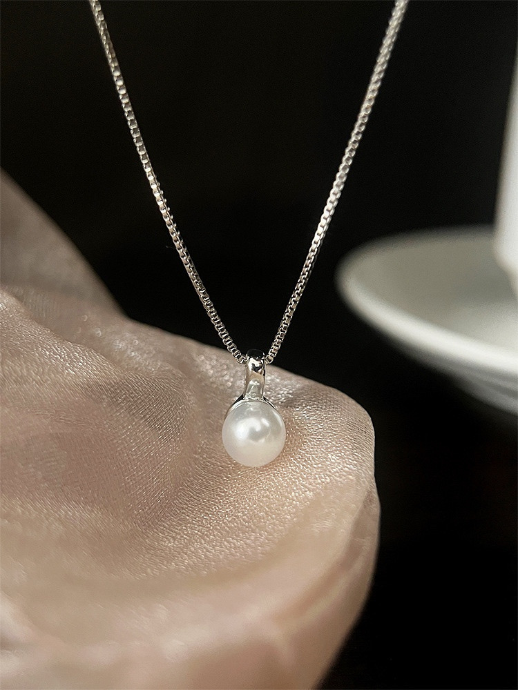 Close-up of a white faux pearl pendant on a silver-tone chain against a dark background