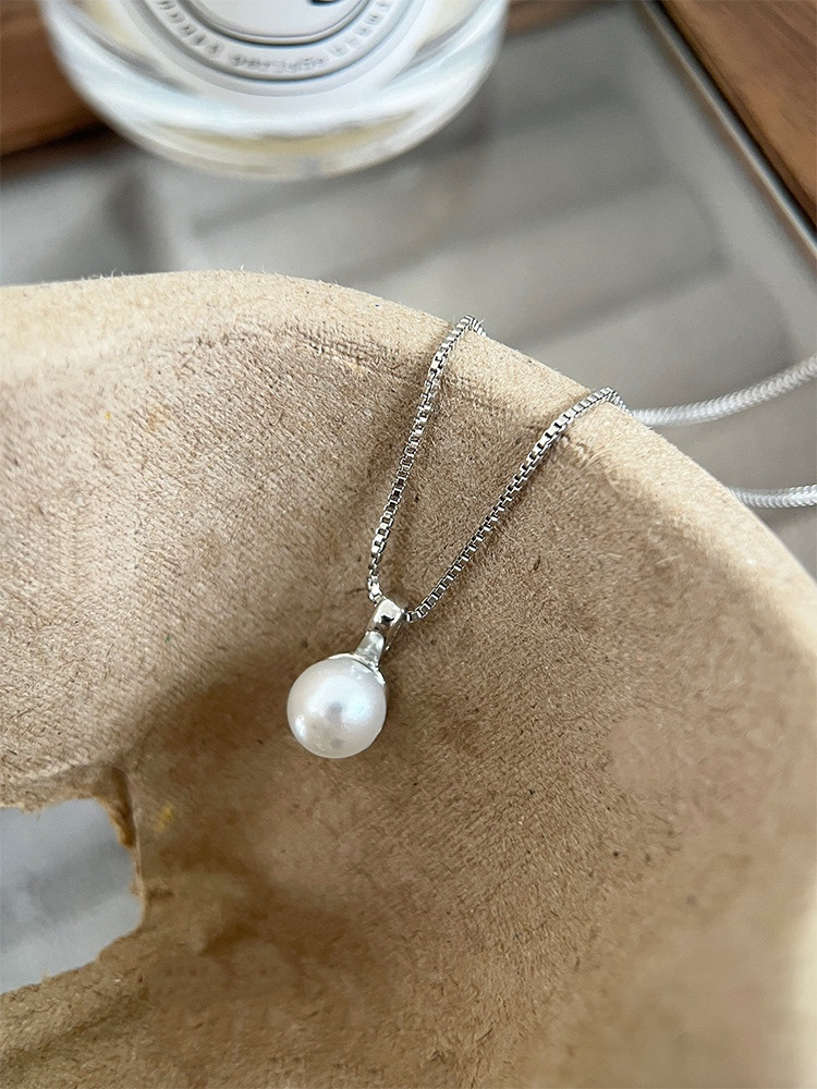 Minimalist silver faux pearl necklace displayed on soft beige fabric