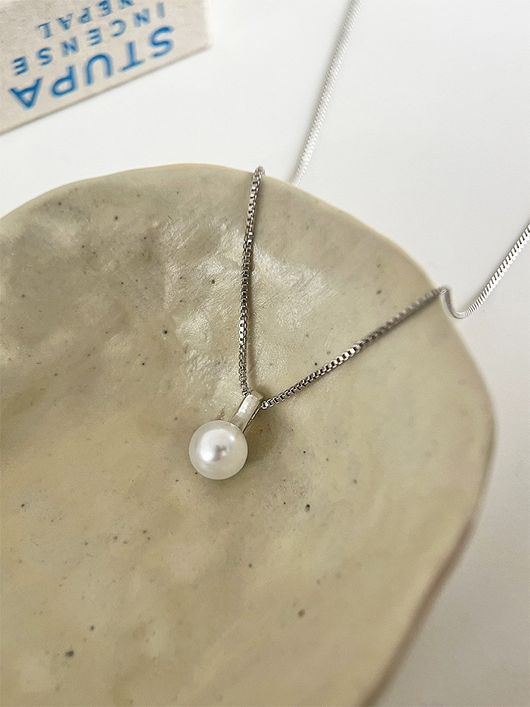 Silver faux pearl pendant necklace displayed on a light ceramic plate