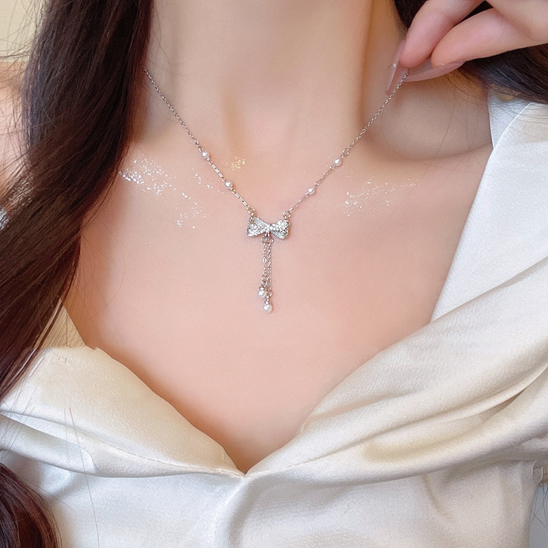 Woman wearing a silver zircon bow pearl tassel necklace with an elegant white outfit