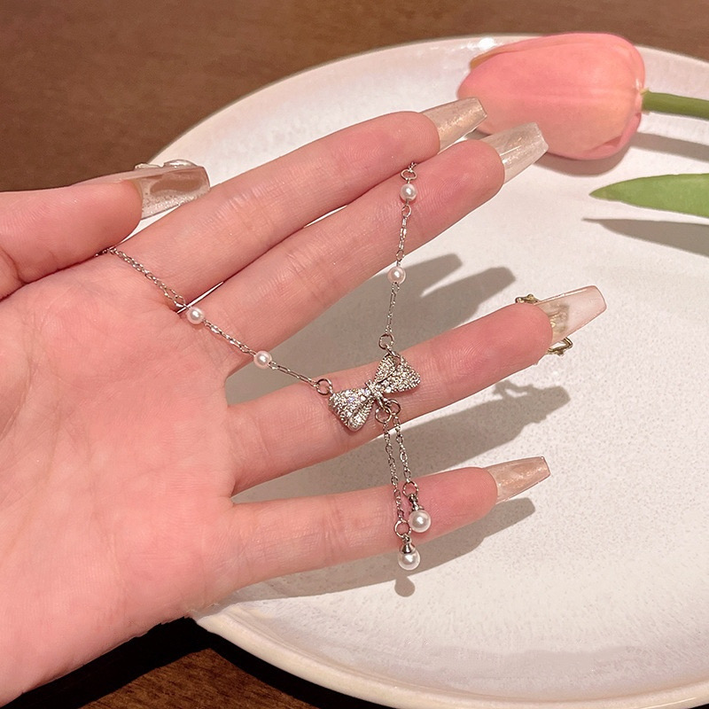 Close-up of silver zircon bow pendant necklace with dangling white faux pearl tassels displayed in hand