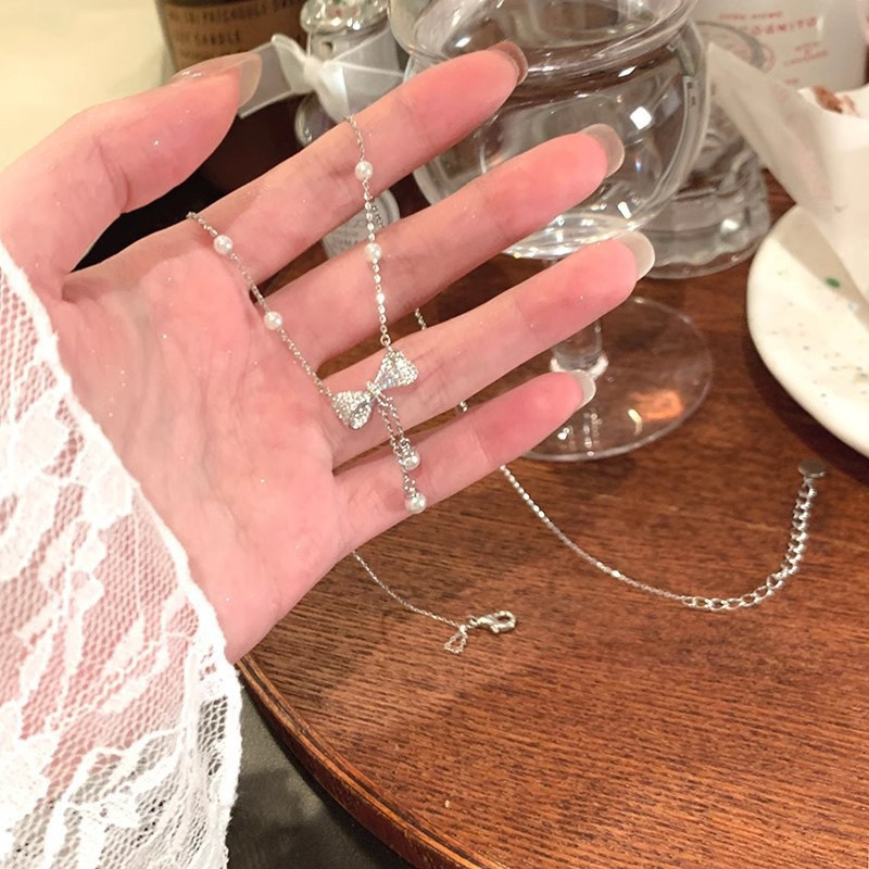 Silver-tone zircon bow necklace with white pearl tassels and delicate chain displayed in hand