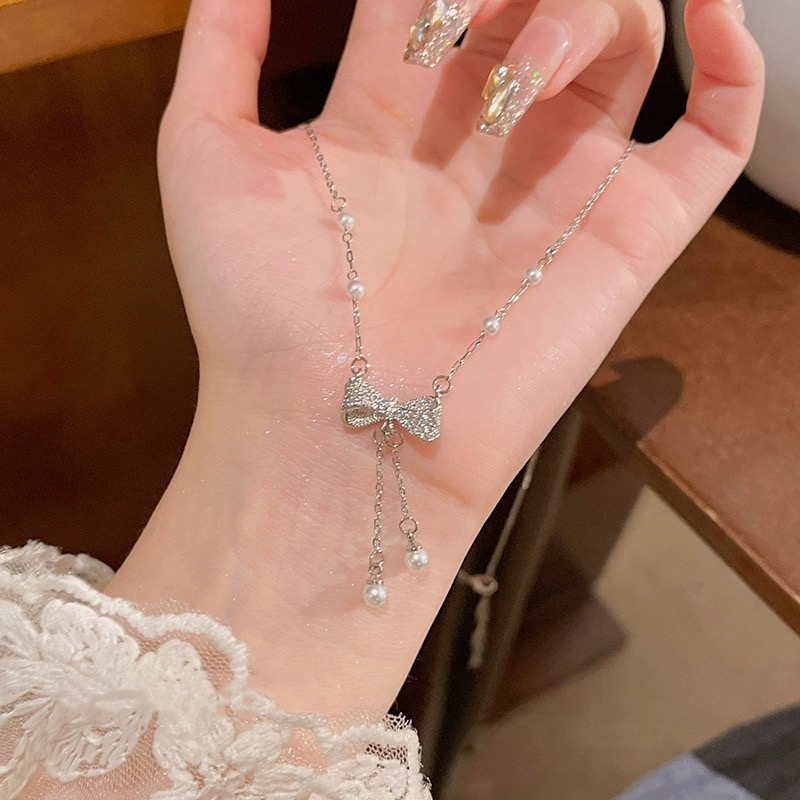 Detailed view of silver zircon bow pendant with two dangling faux pearl tassel chains