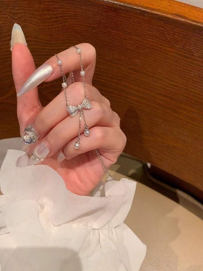 Hand holding a silver-tone zircon bow necklace with delicate pearl tassel chains