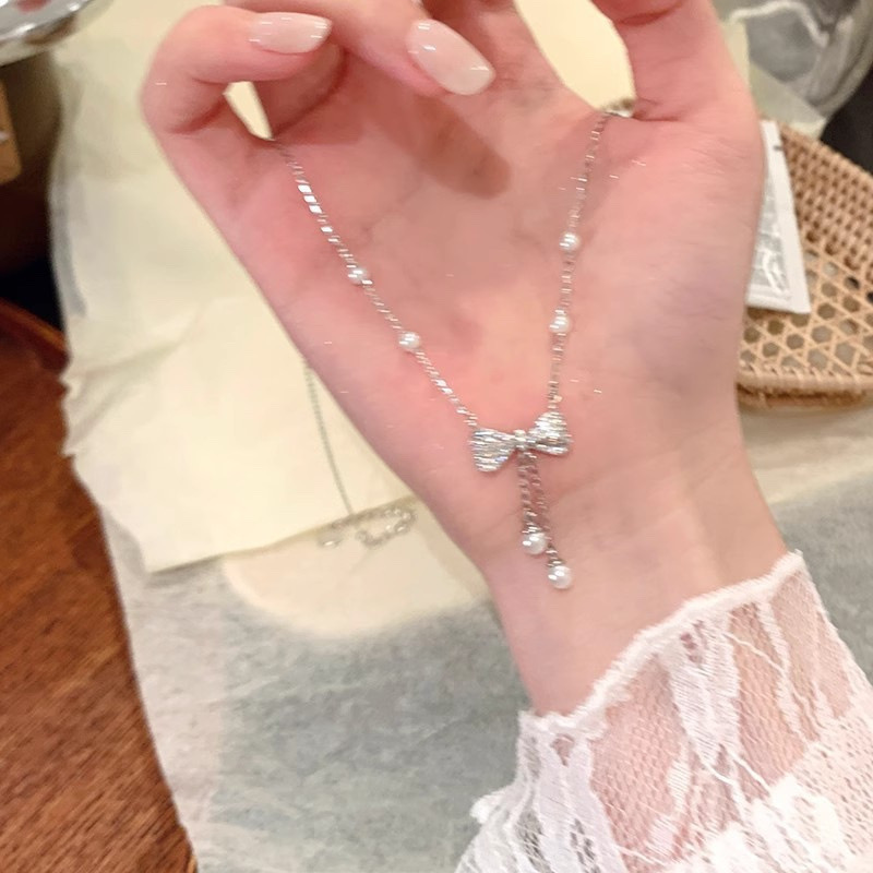 Silver bow pearl tassel necklace displayed across an open hand showing its delicate chain and pendant
