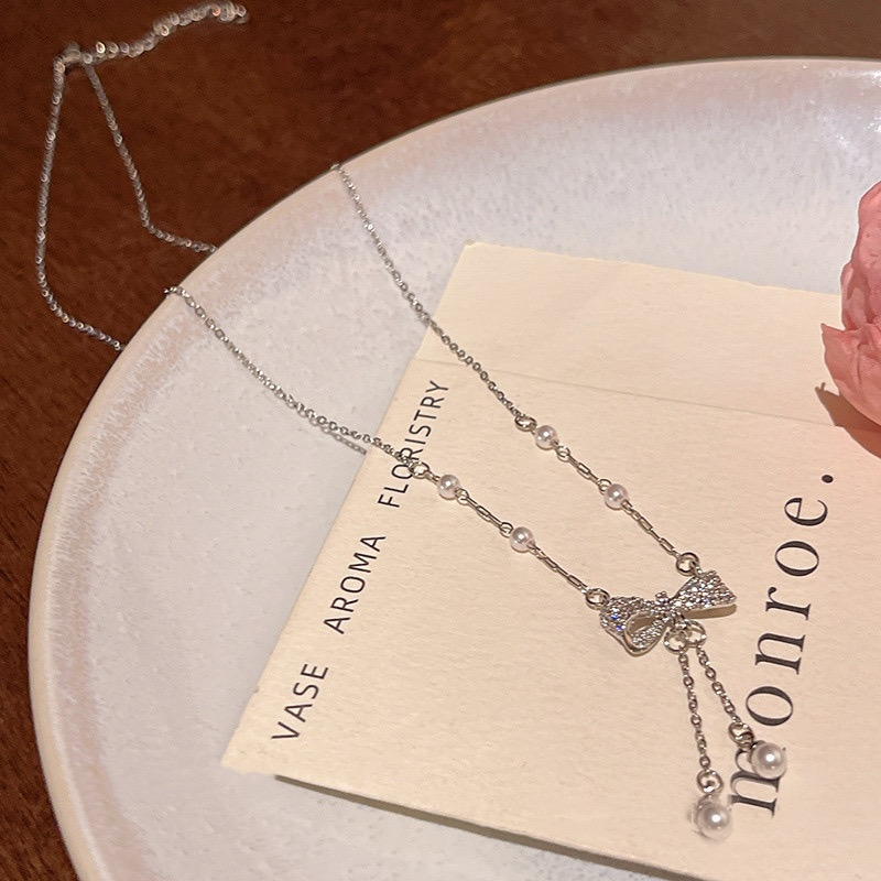 Silver zircon bow pearl tassel necklace displayed on a white plate with delicate chain details