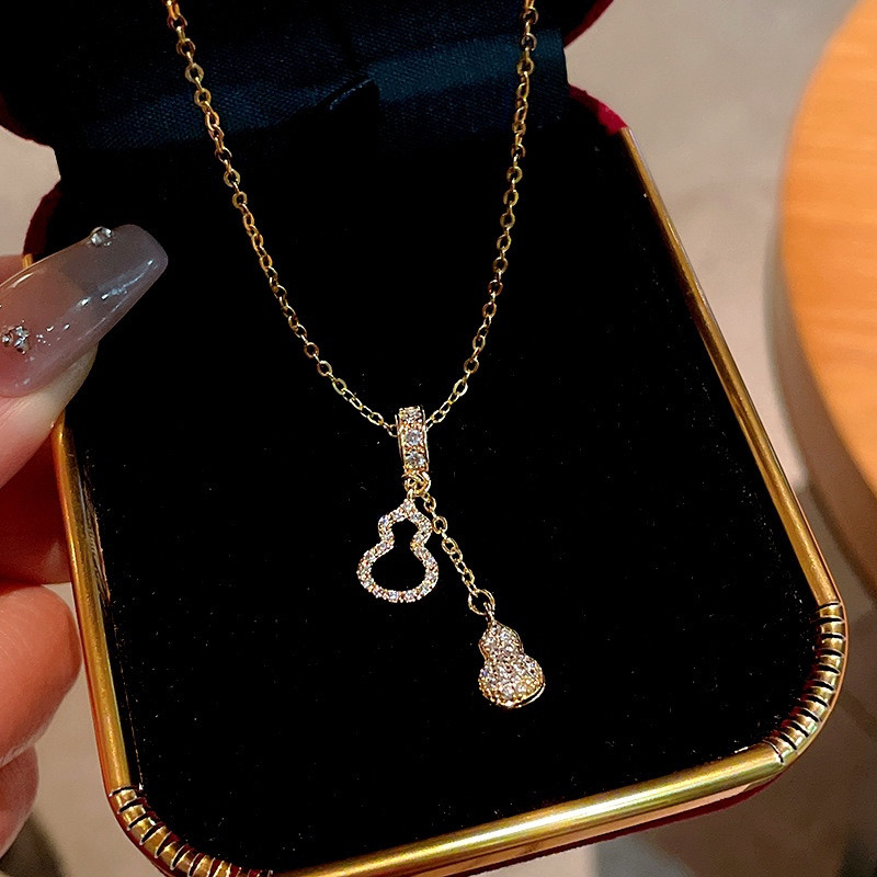 Close-up of gold-tone zircon necklace with sparkling gourd-shaped pendant and dangling charm