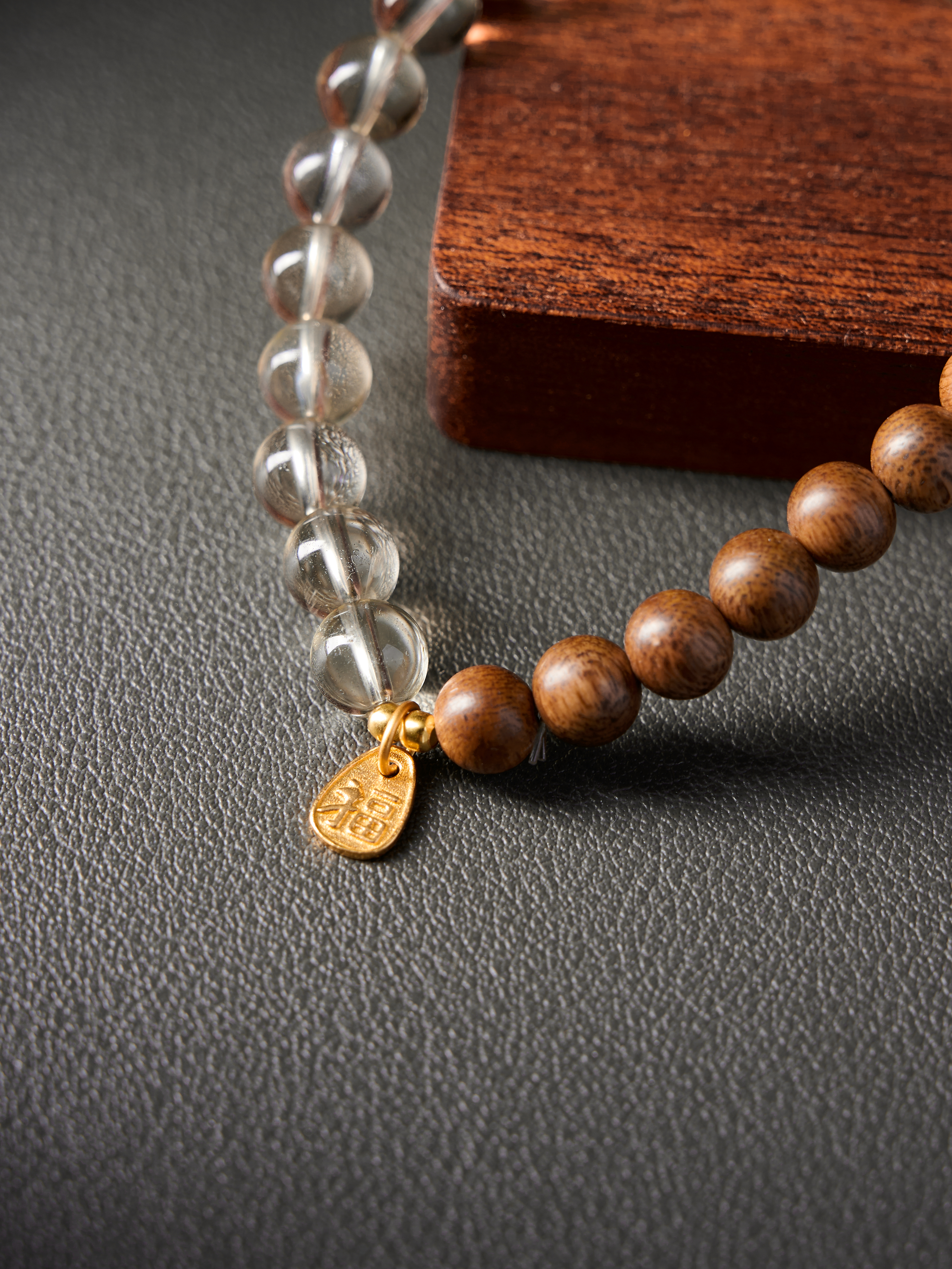 Extreme detail of gold charm and knot finish with transition between crystal and sandalwood beads
