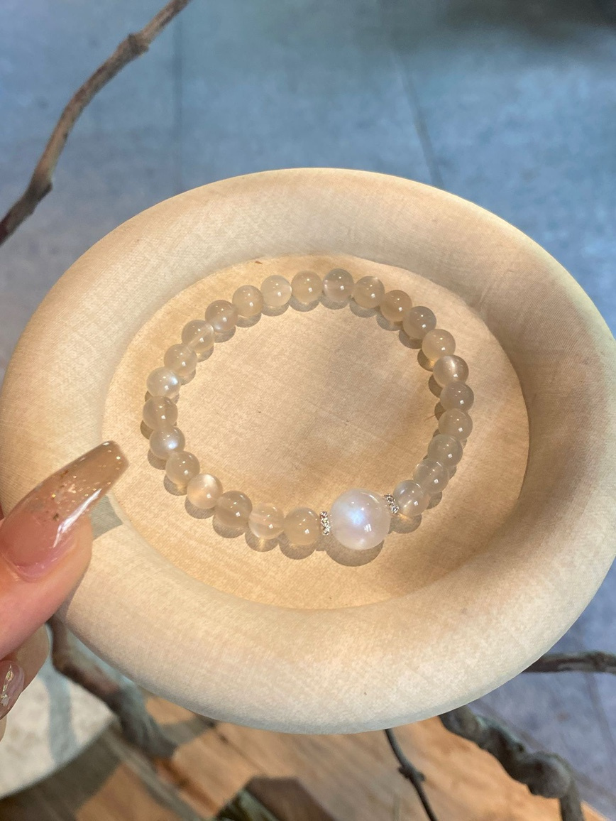 Main view – natural moonstone bracelet with soft white glow on wooden plate.