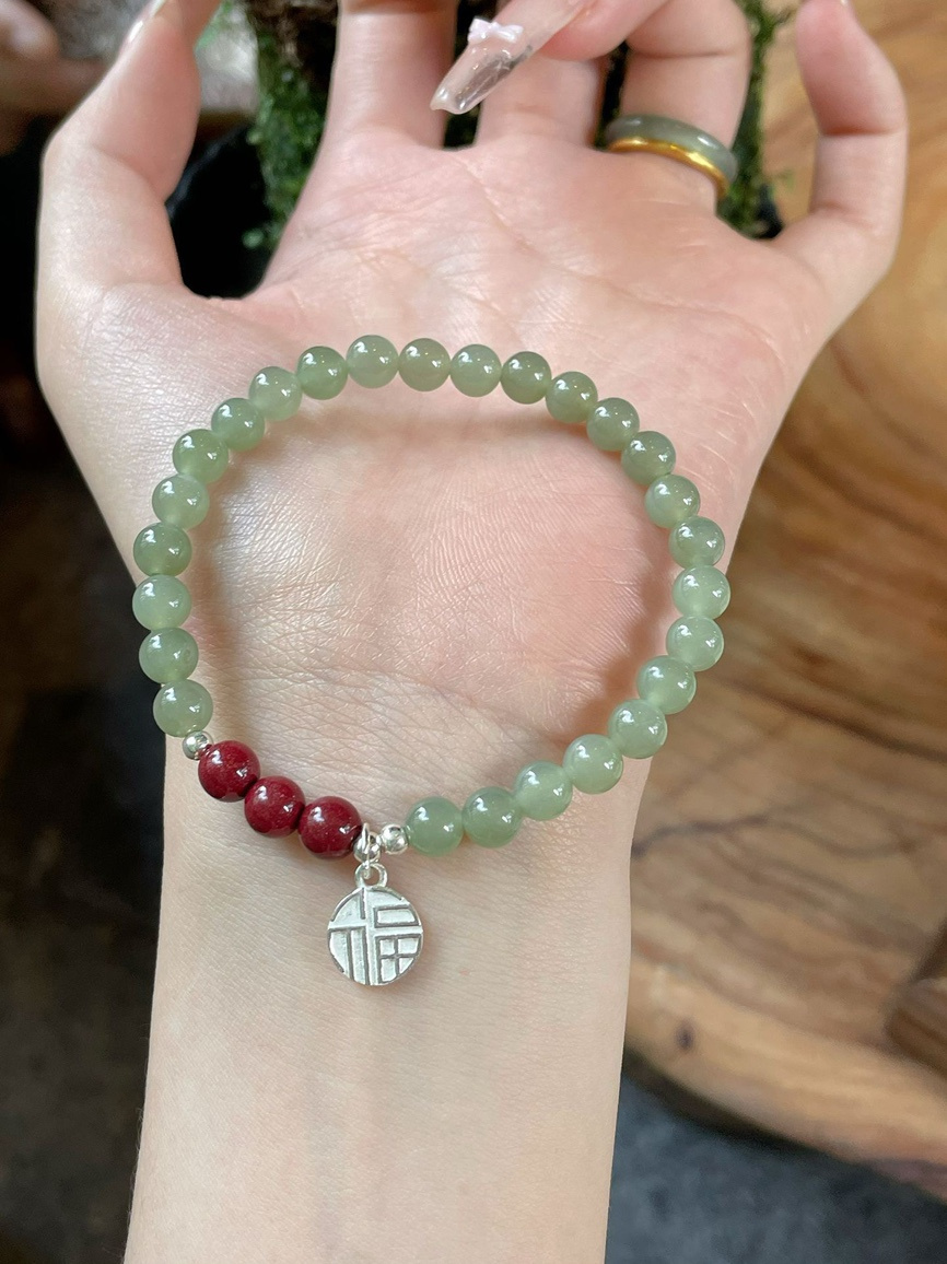 Hand wearing jade and cinnabar bracelet under soft natural light