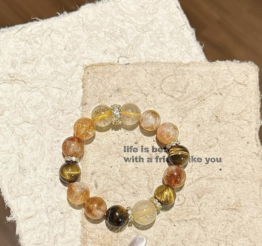 Golden rutilated quartz, citrine, and tiger’s eye bracelet on a textured paper background