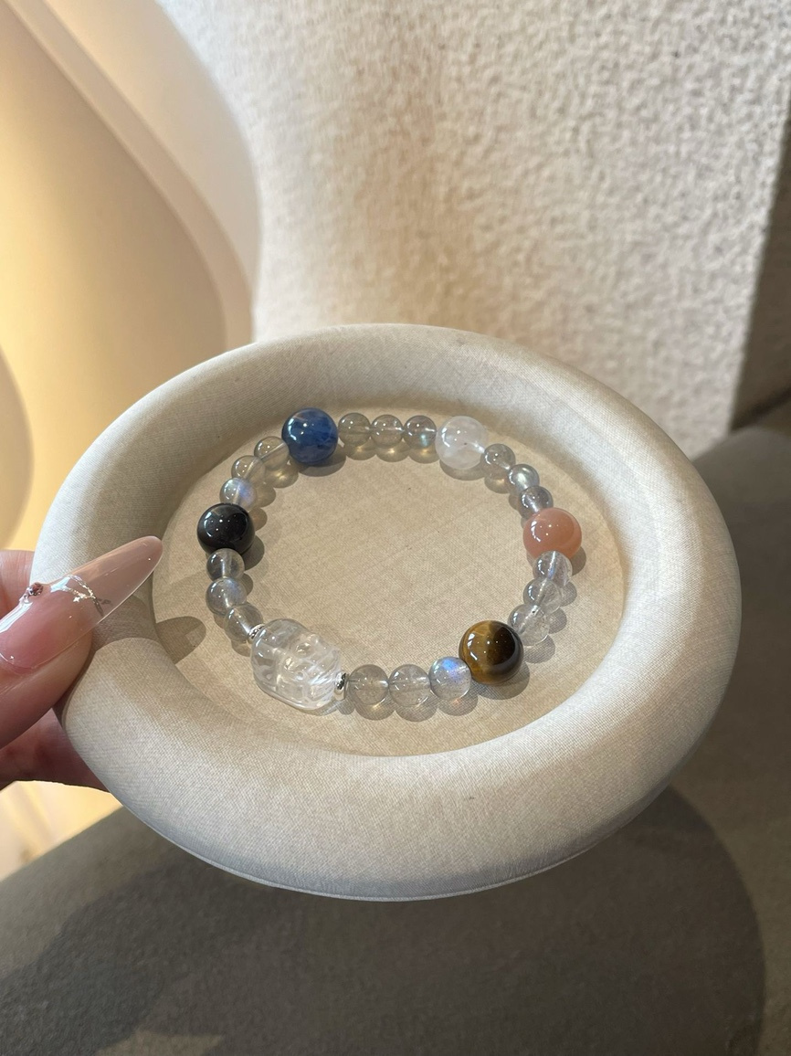 Close-up of clear quartz, grey moonstone, white sunstone and tiger’s eye bracelet on round display tray.
