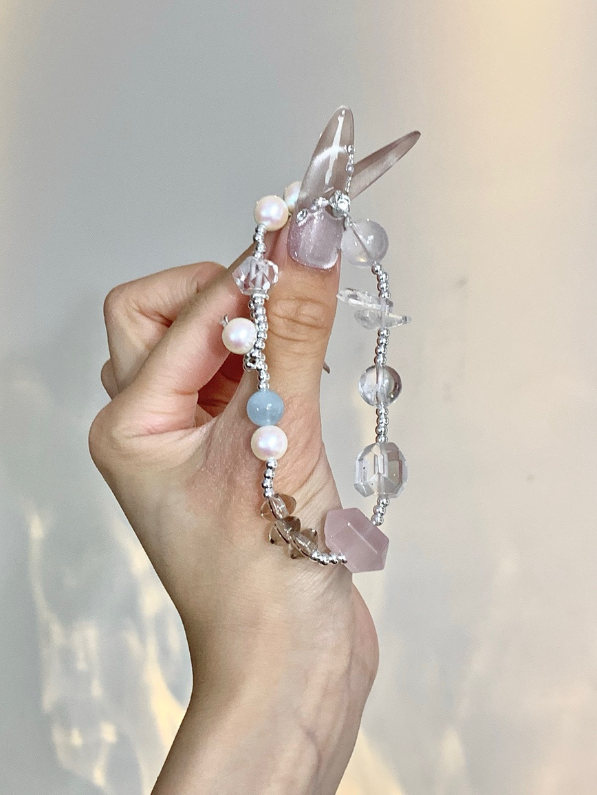 Natural crystal bracelet with pearl and rose quartz displayed in hand — elegant lighting.