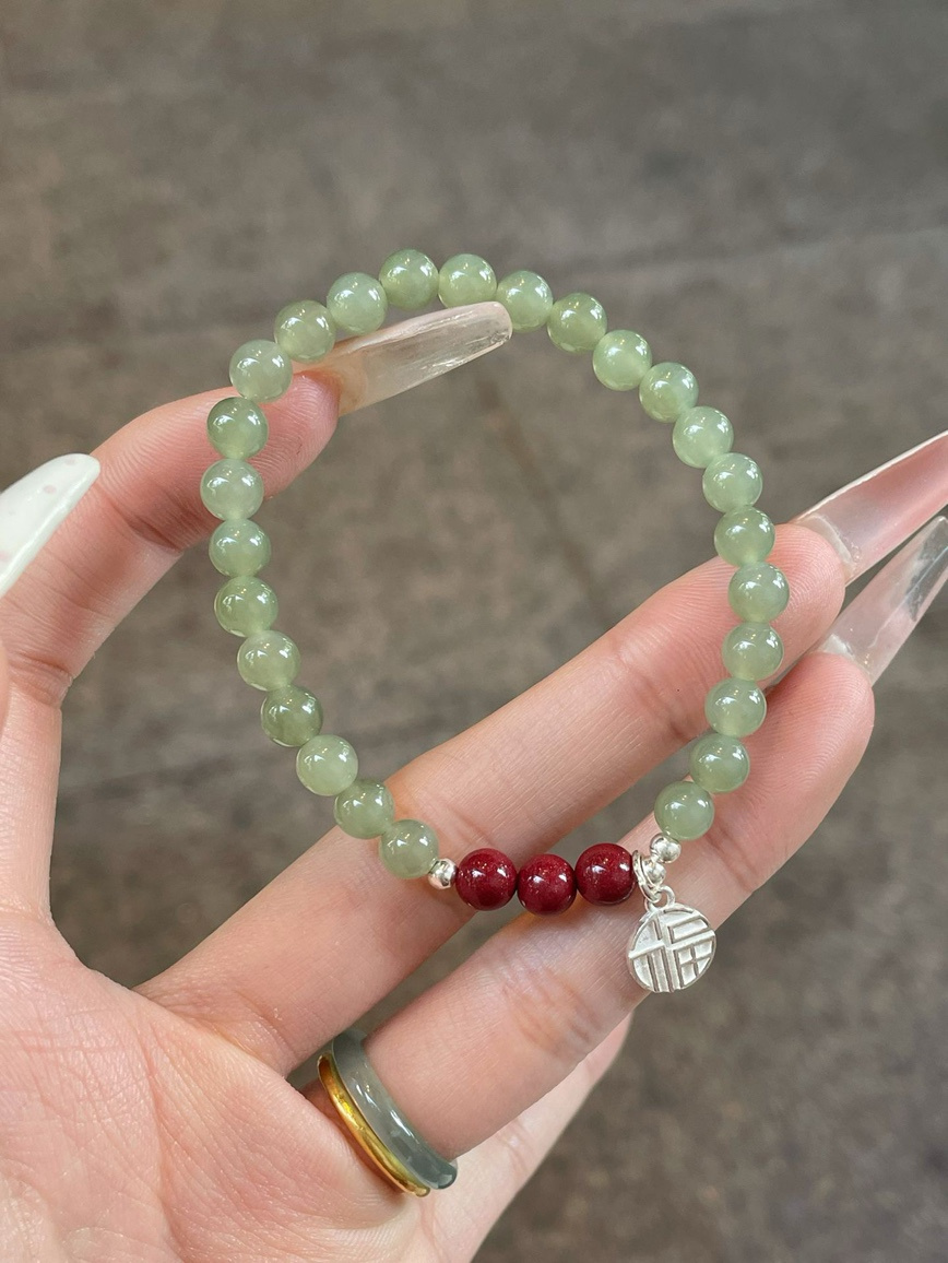 Close-up of green jade and red cinnabar beads with silver blessing charm