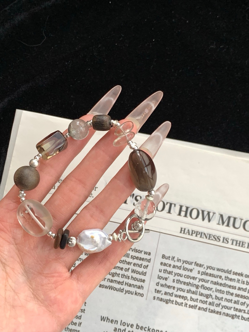 Hand holding clear quartz and baroque pearl bracelet above newspaper
