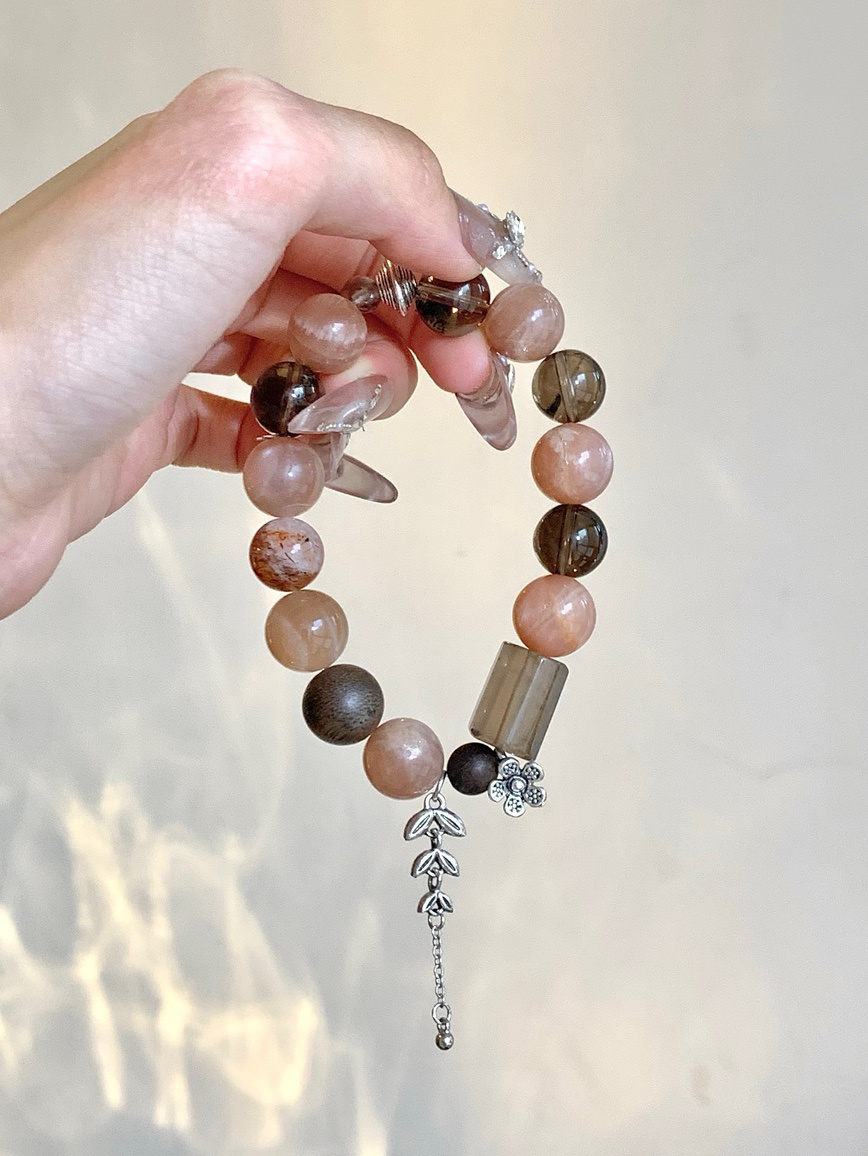Hand holding moonstone and smoky quartz bracelet in soft light
