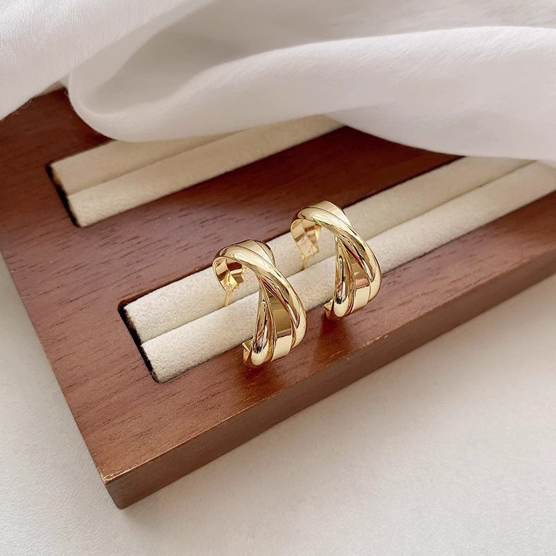 Gold sculptural hoop earrings displayed on jewelry stand