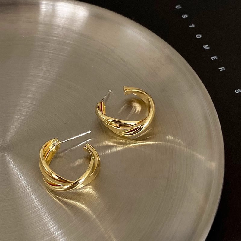 Gold intertwined hoop earrings on white plate