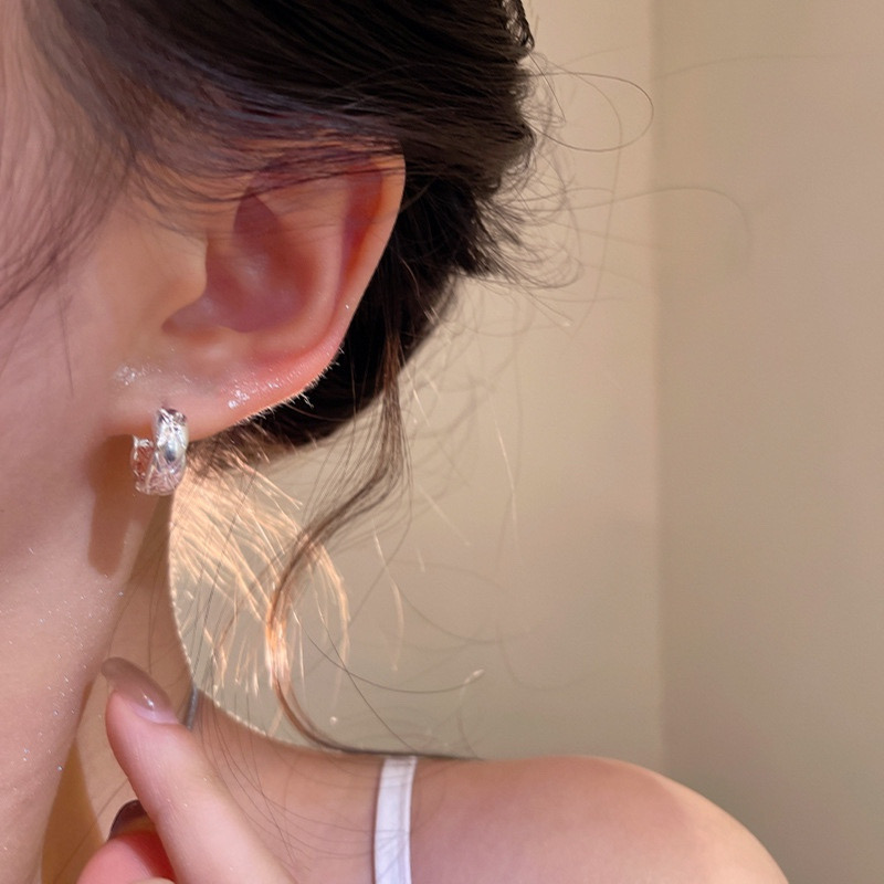 Silver textured woven hoop earrings worn on ear
