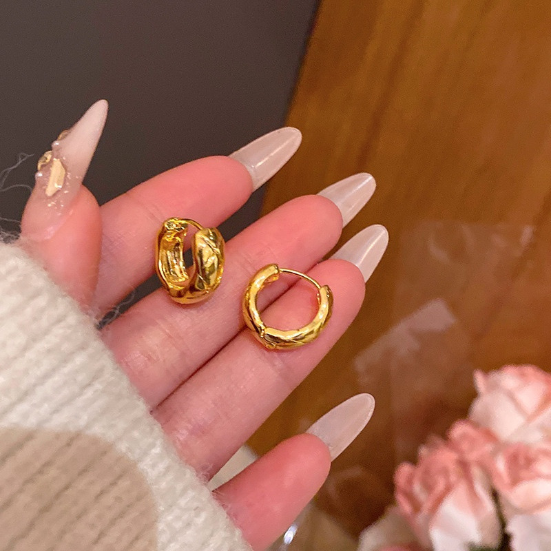 Gold textured hoop earrings held in hand