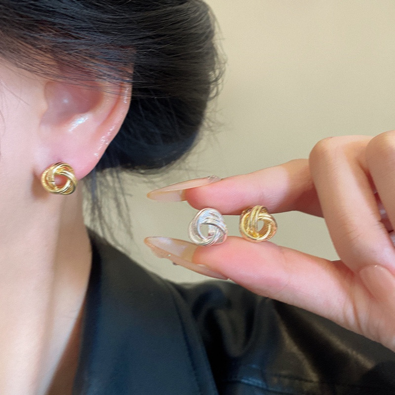 Gold and silver knot stud earrings worn and held in hand