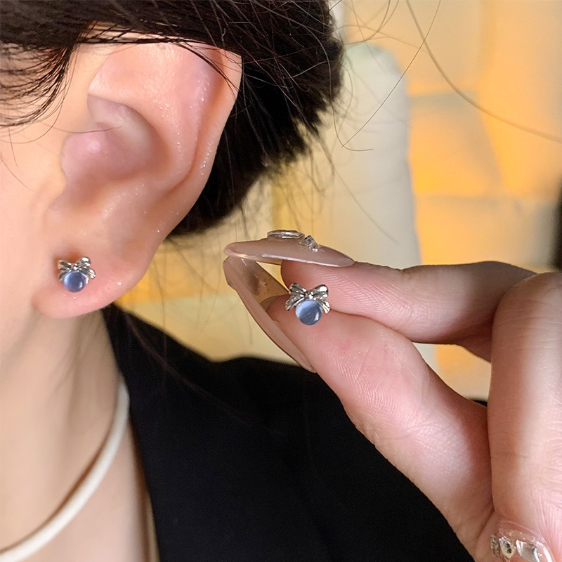 Blue cat eye bow stud earrings worn and held in hand