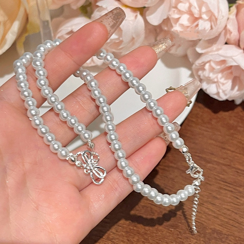 White Faux Pearl Bow Necklace Held in Hand Showing Silver Tone Charm and Adjustable Chain