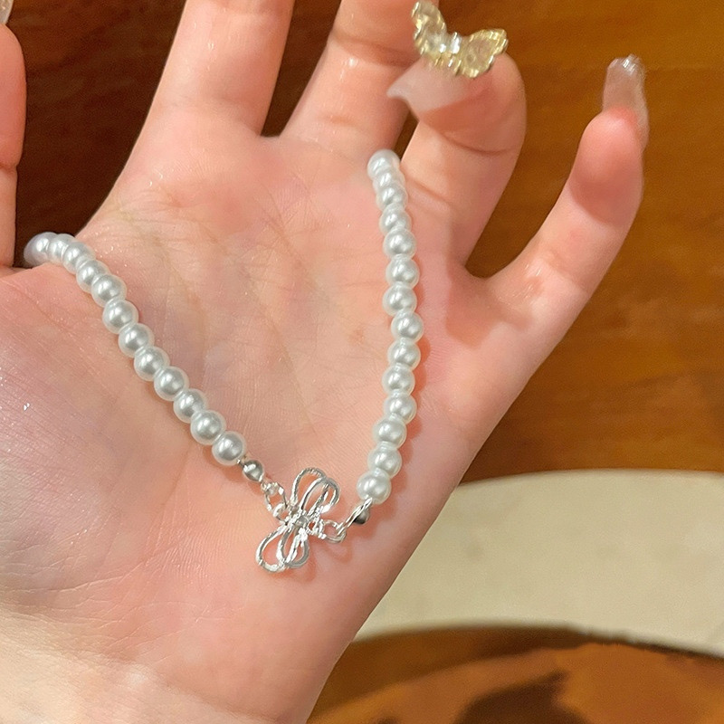 Close Up of White Faux Pearl Necklace with Silver Tone Bow Pendant in Hand
