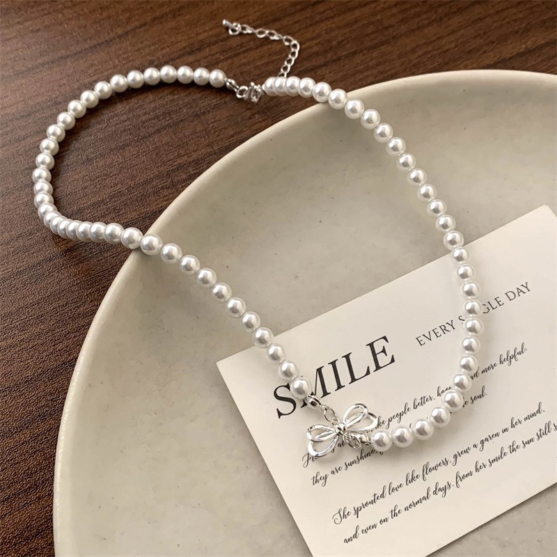 White Faux Pearl Choker Necklace with Silver Tone Bow Charm on Decorative Tray