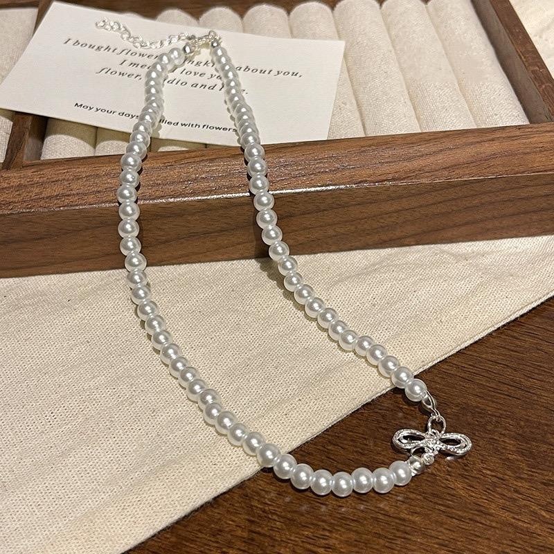 Adjustable White Faux Pearl Choker Necklace with Silver Bow Accent on Fabric Display