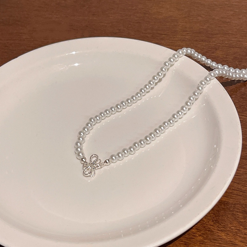 White Faux Pearl Choker Necklace with Silver Bow Detail Displayed on White Ceramic Plate