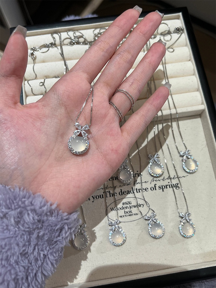 Hand Holding Silver Floral White Stone Pendant Necklace Above Jewelry Display Tray