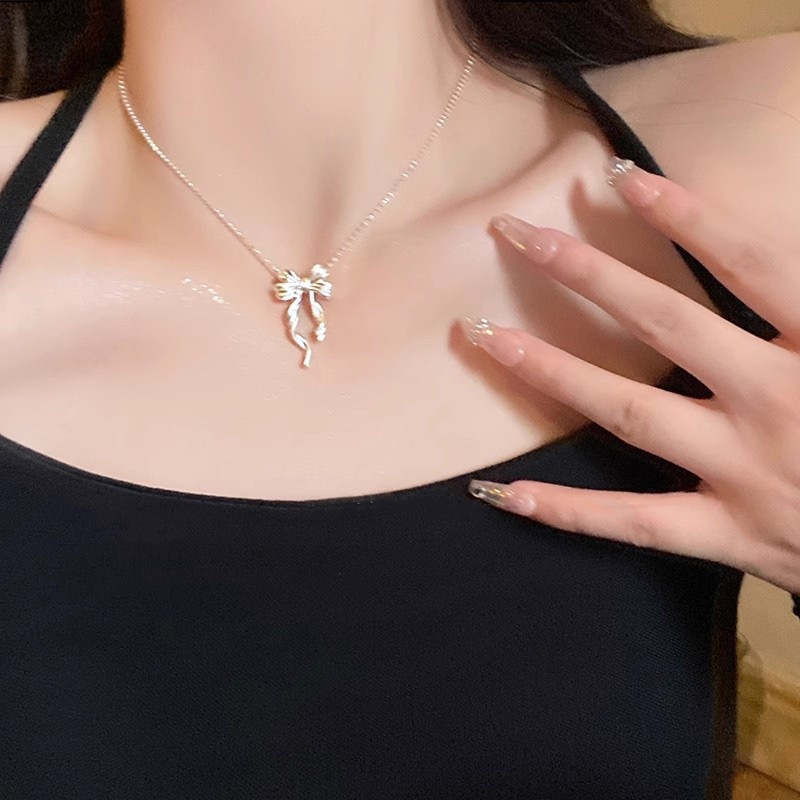 Silver ribbon bow pendant necklace worn with a black sleeveless top, showing its delicate and feminine style